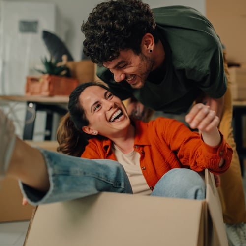 happy woman sittng in moving box with husband in new home