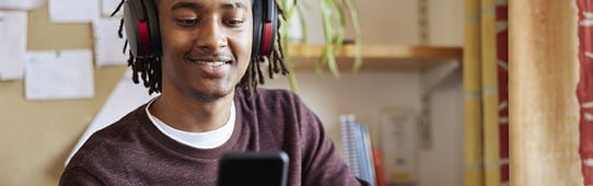 African American male university or college student with headphones looking at cellphone