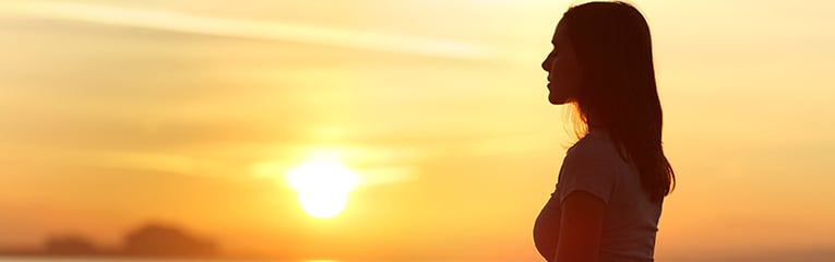 Backlit of woman sitting on the beack in mediation with the sunsetting behind her