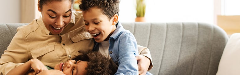 Boy and gril with their mother laughing together on sofa at home
