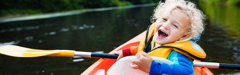 Child riding in a boat with both hands in the air