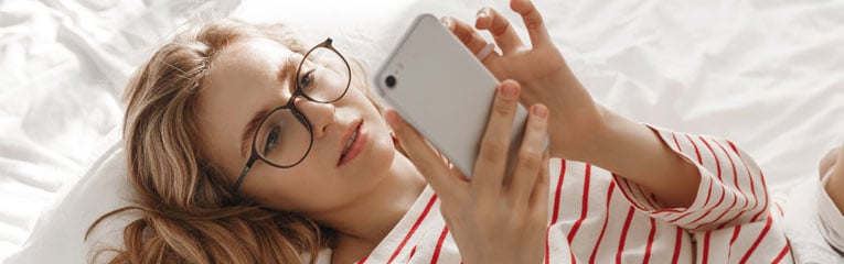 First-time-car-buyer-young-lady-in-glasses-researching-car-loan-fees-on-her-cell-phone.
