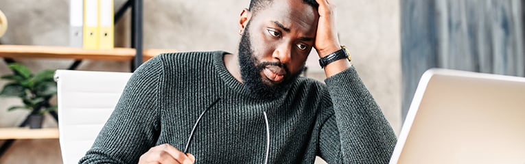 Frustrated sad black guy is watching at laptop screen