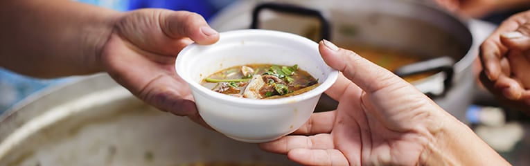 Hands serving soup at homeless kitchen