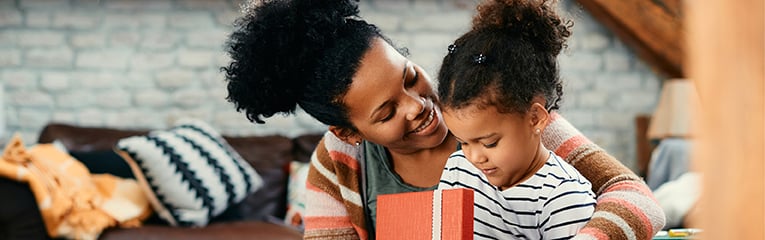 Happy black mother and daughter opening a gift box together at home.