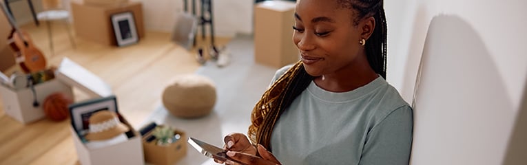 Happy black woman using mobile phone after moving into new home.