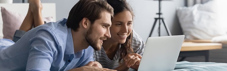 Interested young couple lying on bed, looking at computer screen