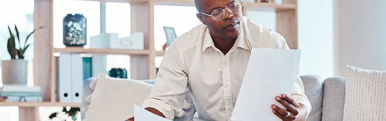 Man reading paperwork in living room home for planning, budget report and investment contract