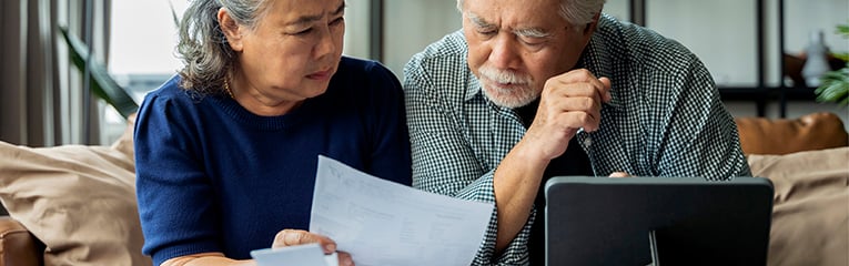 Old retired asian senior couple checking and calculate financial billing together on sofa involved in financial paperwork