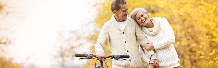 Senior couple walking bicycle in  the forest during the fall smiling