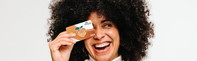 Woman holds PSFCU visa debit card towards face while smiling