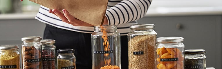 Woman pouring red lentils from paper bag into glass jars