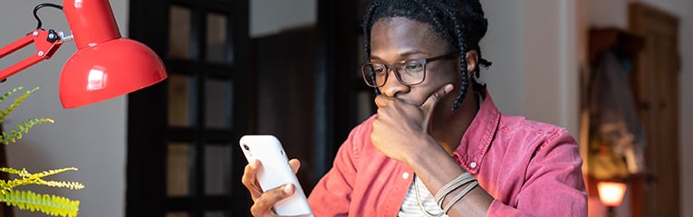 Worried upset young African American man checking phone while working sitting at desk