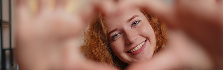 Young redhead woman makes heart hands