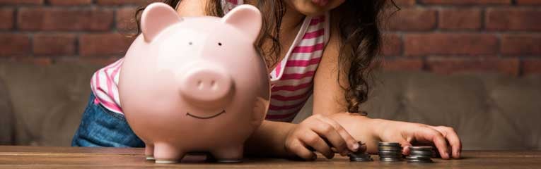 a kids-savings-account-helps this young girl have savings goals as she counts her change by her piggy bank