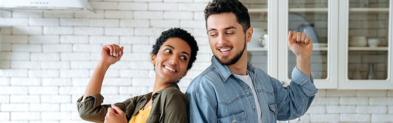 Caucasian man and african american woman are having fun, dancing while making fresh healthy salad for a lunch