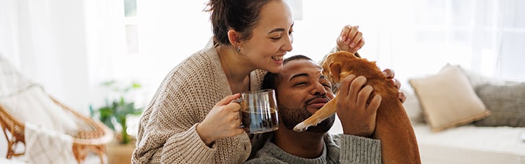 Cheerful young interracial couple with coffee playing with chihuahua dog at home