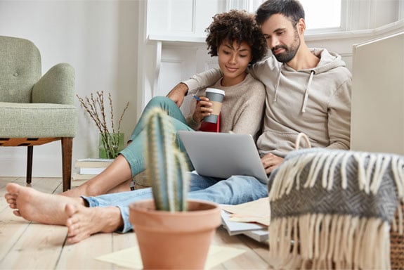 Couple-using-budget-templates-as-they-sit-on-the-floor-together-and-review-their-finances-on-their-laptop.