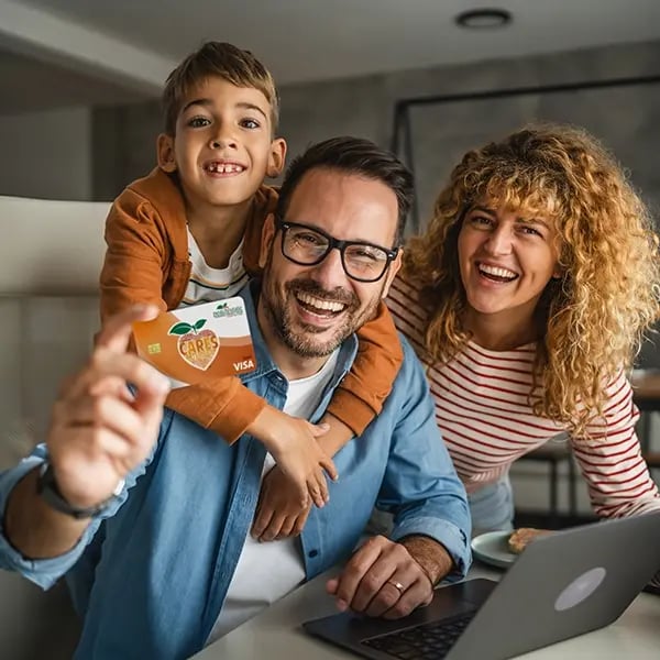 Family smiles in computer room while holding PSFCU visa debit card