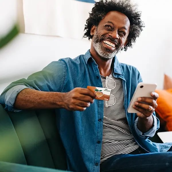 Middle aged man smiles while on his phone holding PSFCU visa debit card