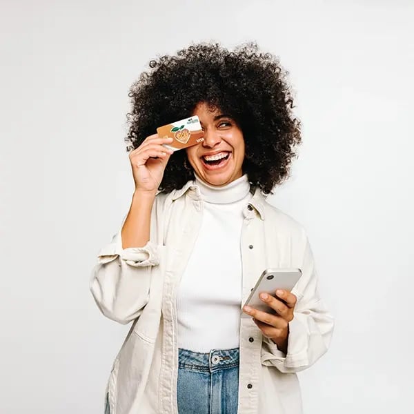 Woman holds PSFCU visa debit card towards face while smiling