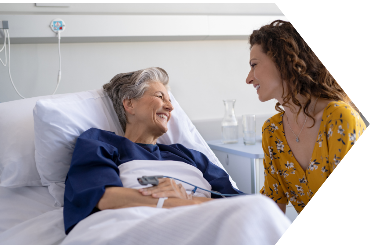 older woman in hospital bed with lovoed one sitting next to her