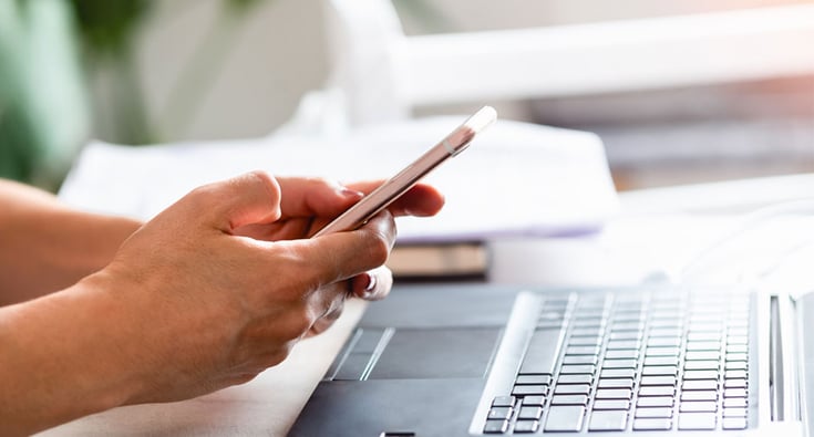Persons-hands-researching-debt-card-safety-measures-while-looking-at-their-cellphone-and-laptap.