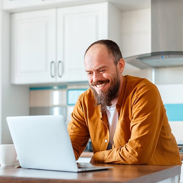 A man in his kitchen logs into Peach State online banking with his laptop.