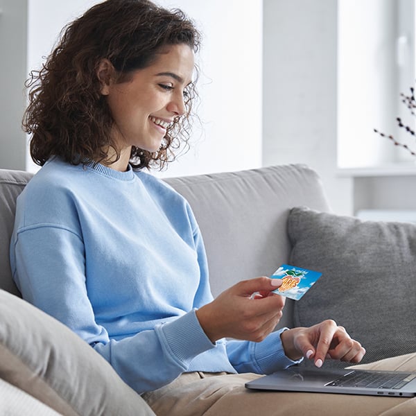 A young woman uses her Peach State C.A.R.E.S. Card to shop online from her couch.