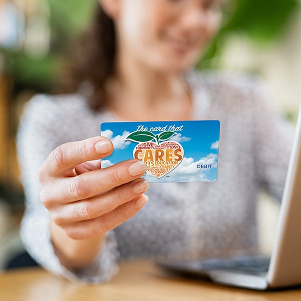 Young lady holds up Peach State debit card while online shopping