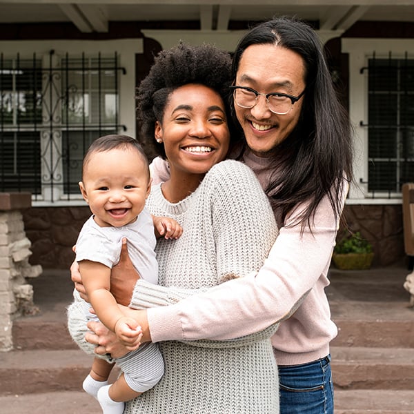 Young new family stands in front of home