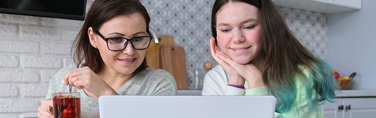 mother and daughter teenager, talking parent and child sitting at home in kitchen and looking at laptop screen