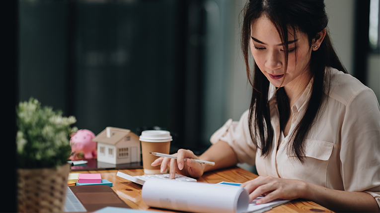 Asian business woman budgeting looking at notepad and typing on calculator