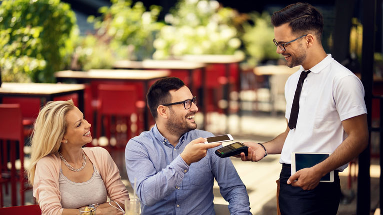 Couple-paying-a-waiter-for-dinner-at-a-resstuarant-using-their-mobile-wallet-on-their-cellphone.