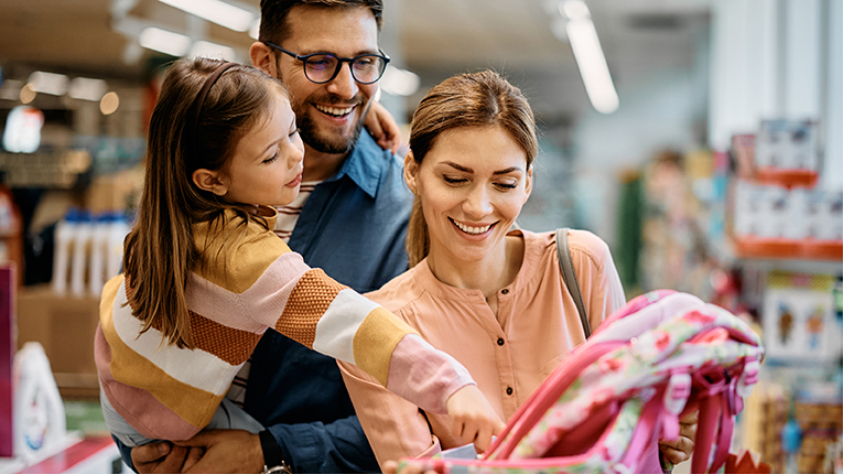Happy little girl pointing at backpack while buying school supplies with her parents