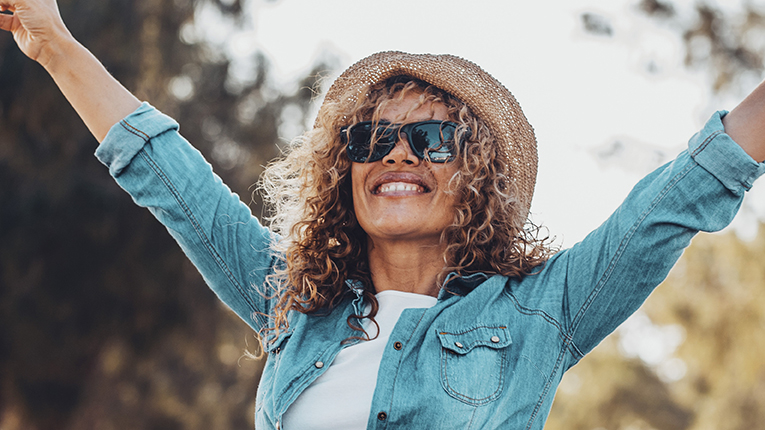 Overjoyed people happy woman raising her arms with victory gesture and smiling with green trees nature outdoors background