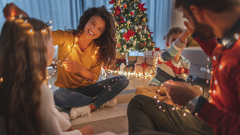 Parents and children smiling by a holiday tree wrapped in holiday lights