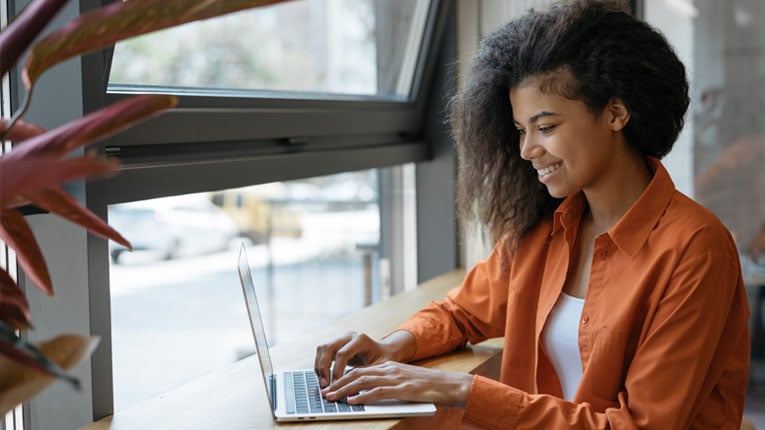 Woman-in-orange-shirt-researching-payment-protection-insurance-options-on-her-laptop.