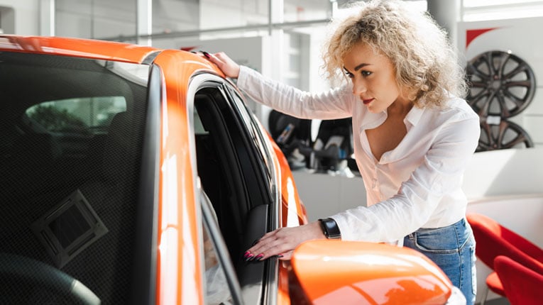 Woman-thinking-of-questions-to-ask-when-buying-a-used-car-as-she-inspects-a-potential-car.