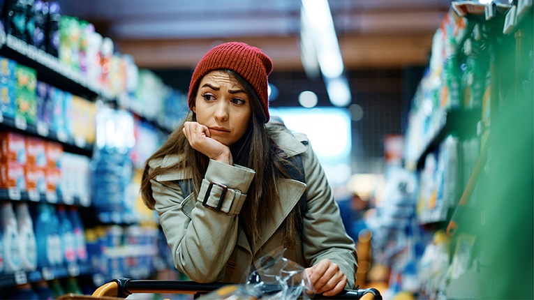 Young woman feeling worried about increase in food prices while buying in supermarket