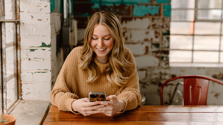 Young-woman-accessing-her-online-and-mobile-banking-on-her-cell-phone-at-a-restaurant.