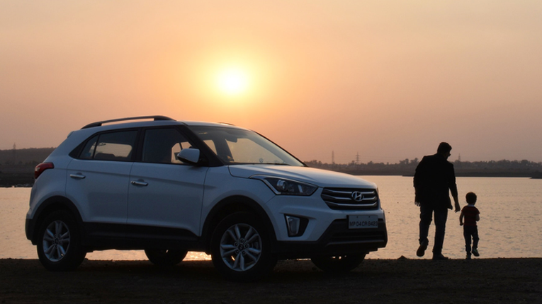 Father and child walking towards water with new car in background.