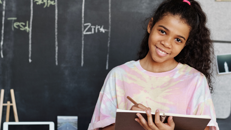 Girl in the classroom holding her notebook smiling.
