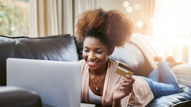 African-american-woman-doing-a-credit-card-balance-transfer-while-laying-on-her-leather-couch-with-her-laptop-and-credit-card.
