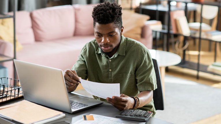 Man-in-green-shirt-is-ready-to-consolidate-debt-after-reviewing-his-monthly-bills-and-his-budget-on-a-laptop.