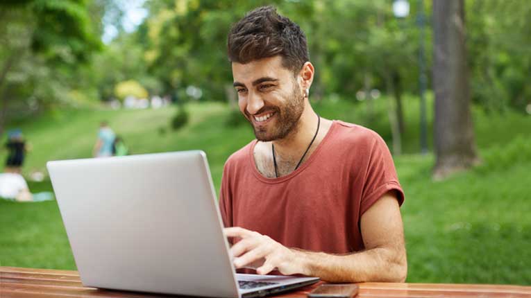 Man-in-red-shirt-researching-how-to-cancel-a-credit-card-correctly-while-on-a-laptop-in-a-park.