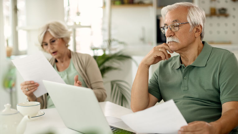 Older-couple-considering-a-bill-consoldation-loan-as-they-review-their-budget-and-bills-on-their-laptop-together.