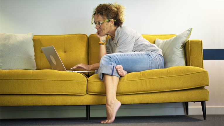 Woman-exploring-consolidation-loans-on-her-laptop-while-sitting-on-yellow-couch.