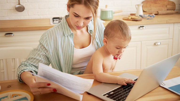 Mom considering a personal loan for debt consolidation as she pays her bills with her baby on her lap.