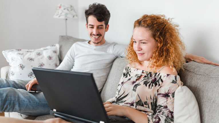 Couple researching arm loan options on their laptop while sitting on a couch.